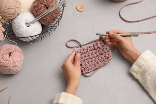 Woman crocheting with threads at grey table, closeup. Engaging hobby