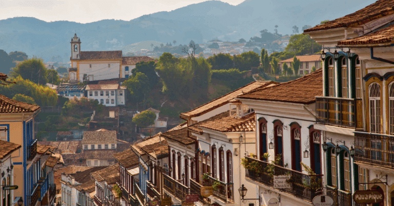 Imagem da rua Rua Conde de Bobadela, rua histórica de Ouro Preto em Minas Gerais, com casarões coloniais coloridos, telhados de cerâmica e igrejas ao fundo cercadas por montanhas.