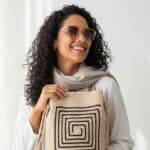 Mulher brasileira sorrindo com bolsa de crochê moderna em tom bege off-white e design min acompanhada de óculos e lenço neutro