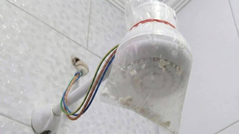 Chuveiro elétrico branco envolto em sacola plástica com resíduos que bloqueavam a pressão da água