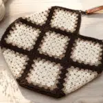 Bolsa feita com quadradinhos de crochê em tons de marrom e bege, com motivos florais e alças compridas.