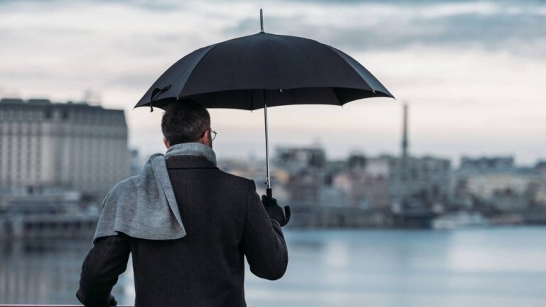 Homem segurando guarda-chuva olhando para paisagem em ponte