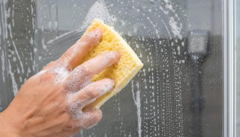 Limpeza de vidro de banheiro com mistura caseira mostrando remoção de sujeira e manchas.