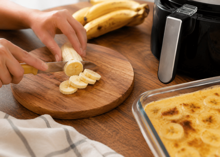 Bananas maduras sendo cortadas sobre mesa de madeira durante o preparo da banana cremosa na Air Fryer.