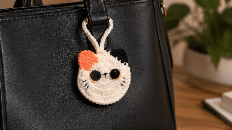 Chaveiro em crochê de gatinho pendurado em bolsa preta, destacando o charme artesanal do acessório feito à mão.