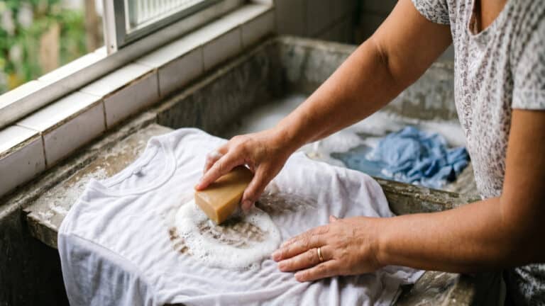 Pessoa esfregando mancha em camisa branca com sabão em barra