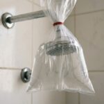 Chuveiro com saco plástico cheio de água preso ao espalhador para ajudar na limpeza.