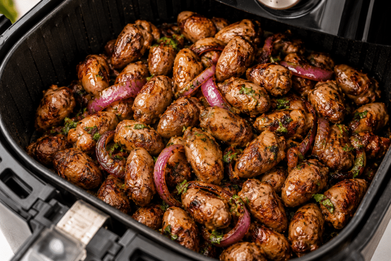 Coração de frango dourado na air fryer com cebola roxa e ervas frescas, pronto para servir como petisco.