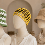 Três manequins sem rosto lado a lado usando chapéus de crochê: um bucket hat verde e branco, um headpiece amarelo vazado e um chapéu bege com flor vinho.