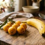 Pequenos frutos amarelos de murici com folhas verdes ao lado de uma banana madura sobre uma tábua de madeira rústica em uma cozinha.