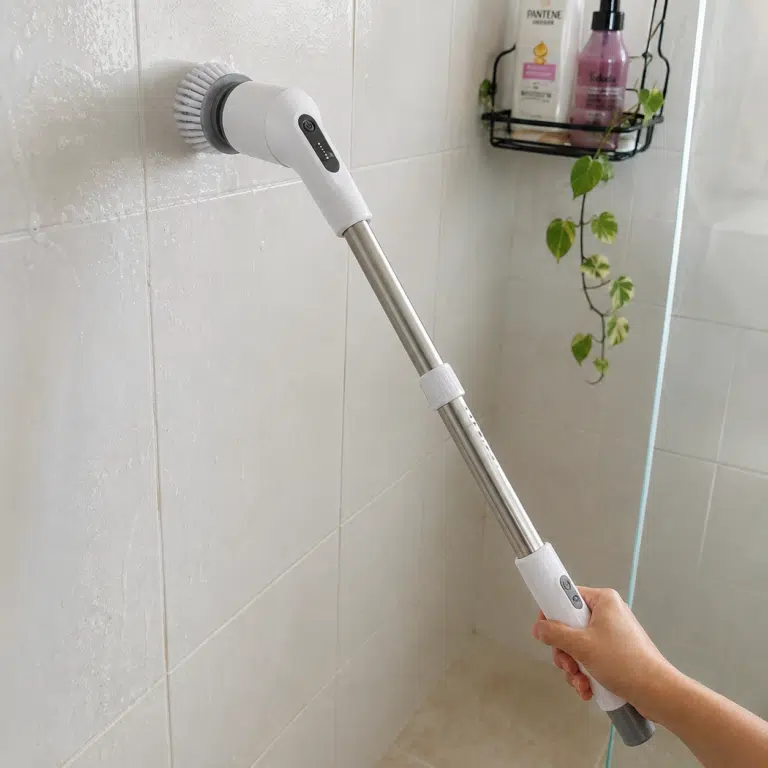 Escova elétrica de limpeza com cabo comprido sendo usada para limpar os azulejos do banheiro.