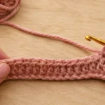 Primeira carreira do crochê repuxando enquanto é trabalhada com fio rosa e agulha de crochê