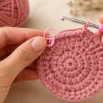 Mãos fazendo crochê circular com marcador de pontos em uma peça rosa