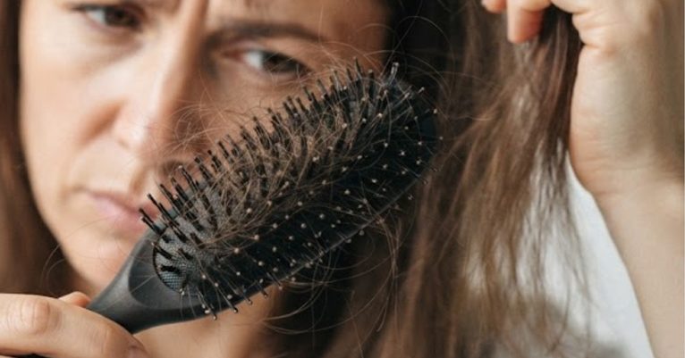 Mulher observa fios de cabelo acumulados na escova após pentear os cabelos.