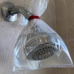 Chuveiro com saco plástico cheio de água preso ao espalhador para ajudar na limpeza.