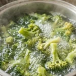 Pedaços de brócolos verdes a cozinhar dentro de uma panela com água a ferver no fogão.